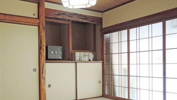 Una habitación con suelo de tatami, una puerta corredera con paneles de vidrio, una pequeña mesa y una lámpara en el techo.