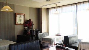 Habitación de hotel con zona de comedor, un sofá, una mesa con mantel rojo y un ventanal con cortinas.