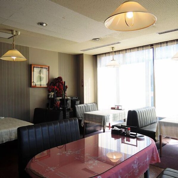 Ein Hotelzimmer mit Essbereich, einer Couch, einem Tisch mit roter Tischdecke und einem großen Fenster mit Vorhängen.
