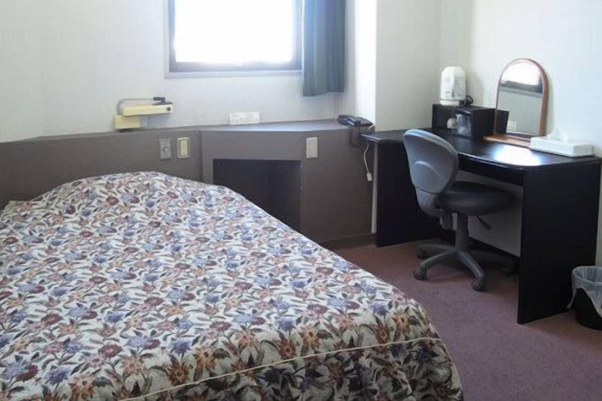 Habitación de hotel con cama, escritorio, silla y ventana con cortinas.