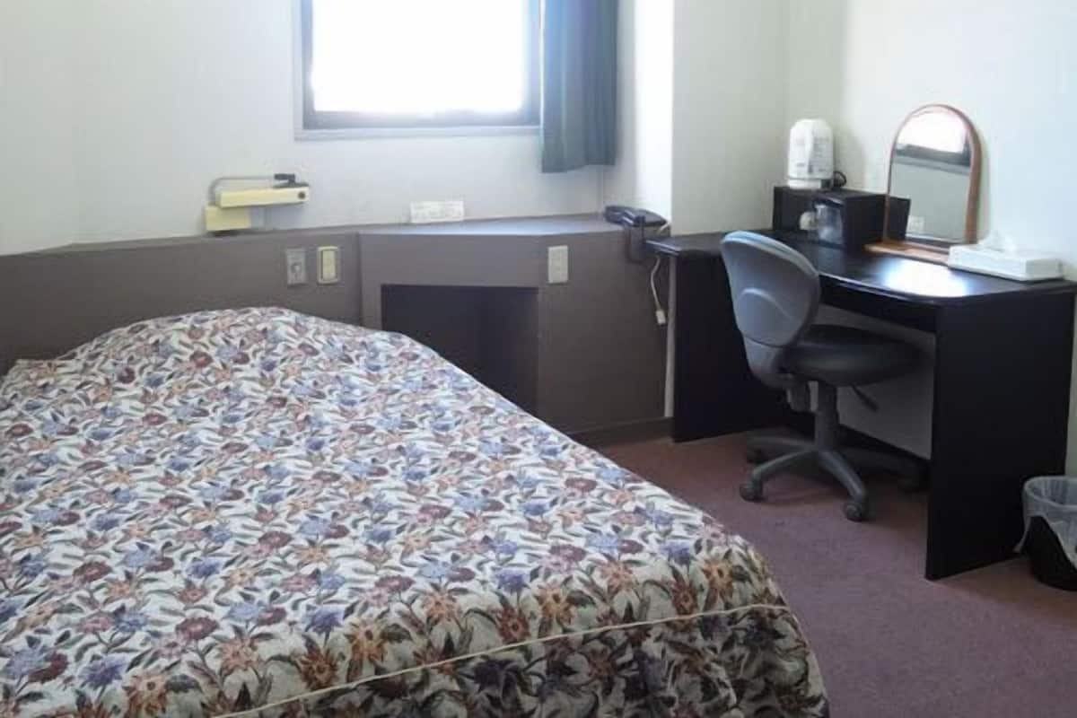 Habitación de hotel con cama, escritorio, silla y ventana con cortinas.