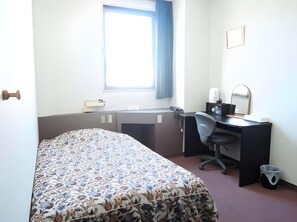 Ein Schlafzimmer mit Bett, Schreibtisch, Stuhl und einem Fenster mit Vorhängen.