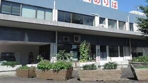 Un edificio con un letrero en japonés, un vestíbulo cubierto y macetas con plantas.