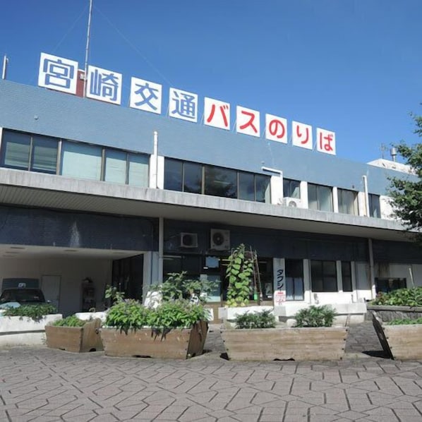 Un bâtiment avec une enseigne en japonais, une entrée abritée et des jardinières remplies de plantes vertes.