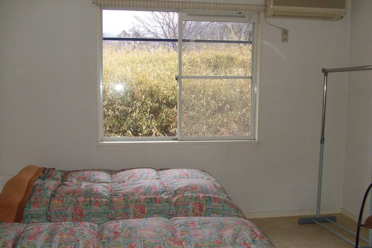 A bedroom with a bed, a window, and a standing fan.