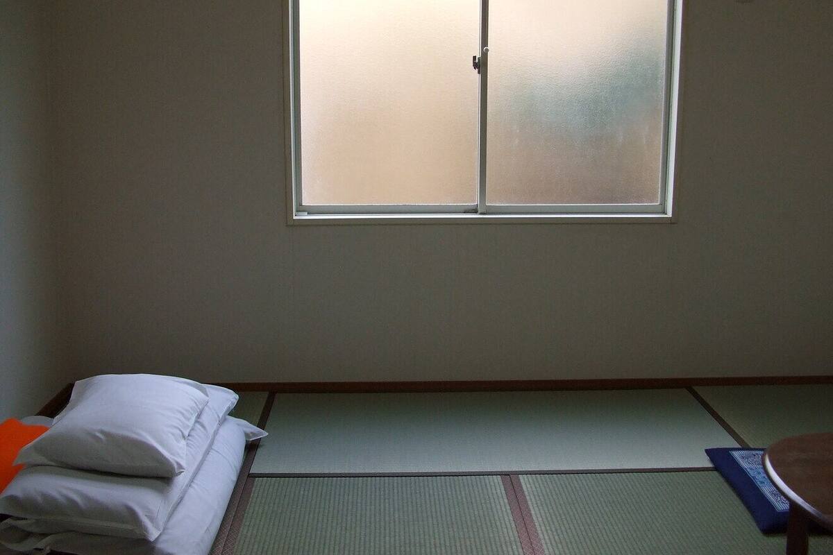 A room with tatami flooring, a futon bed, and a sliding shoji screen window.