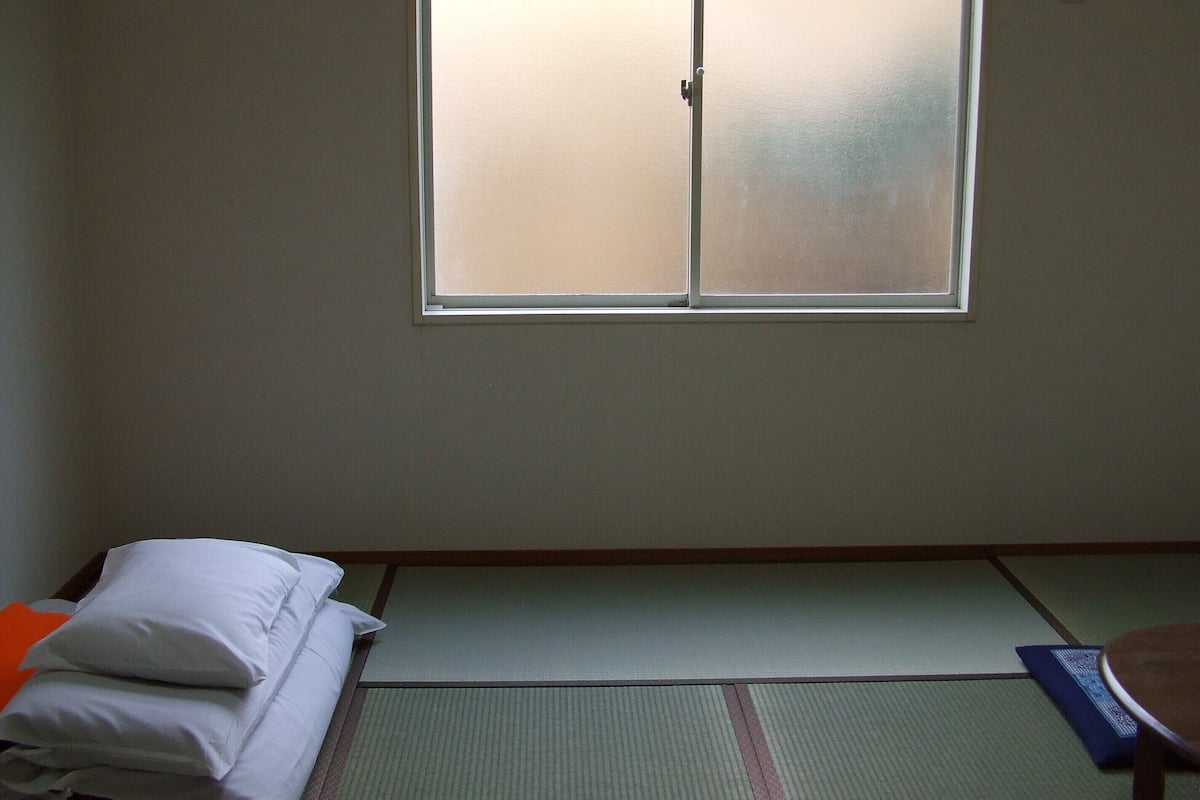 A room with tatami flooring, a futon bed, a window with frosted glass, and a small table.