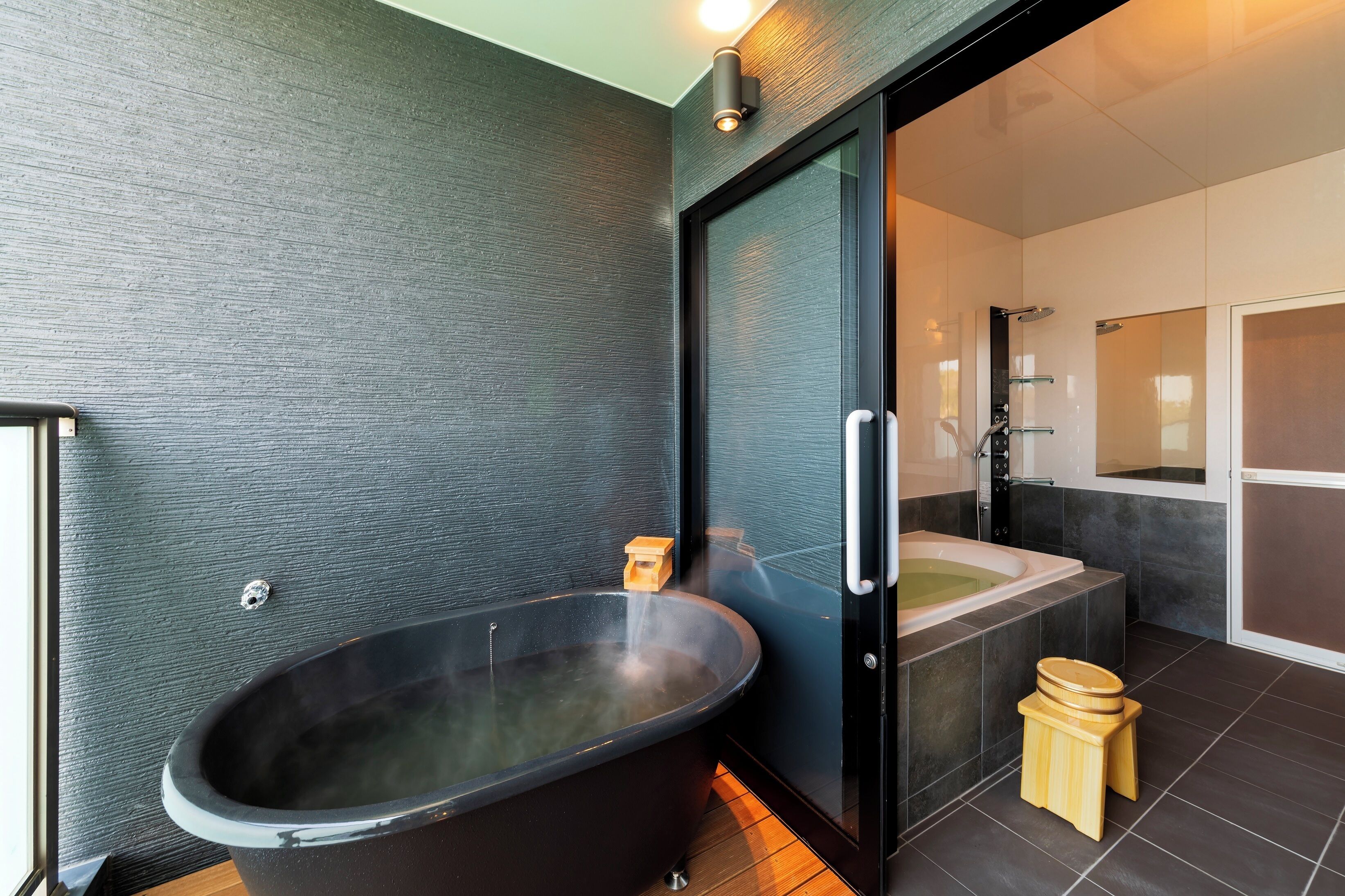 A modern bathroom with a freestanding bathtub, a glass shower enclosure, and a wooden stool.