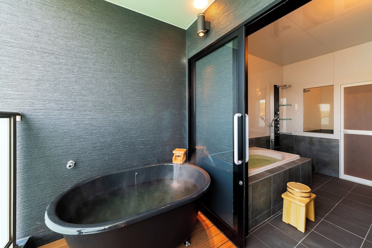 Ein modernes Badezimmer mit einer freistehenden Badewanne, einer Duschkabine aus Glas und einem hölzernen Hocker.