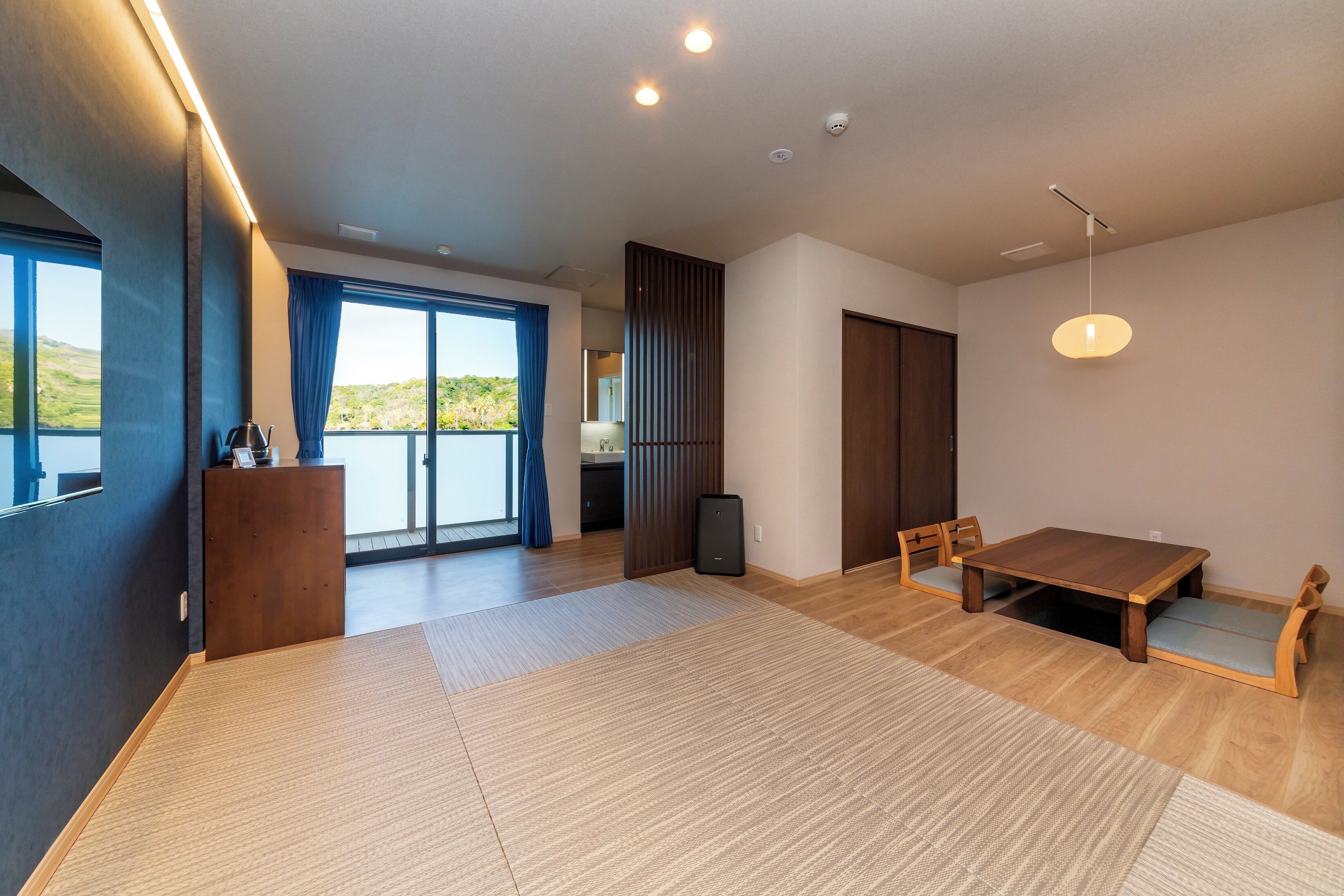 A modern room with a wooden floor, a large table, and a view through a sliding door.
