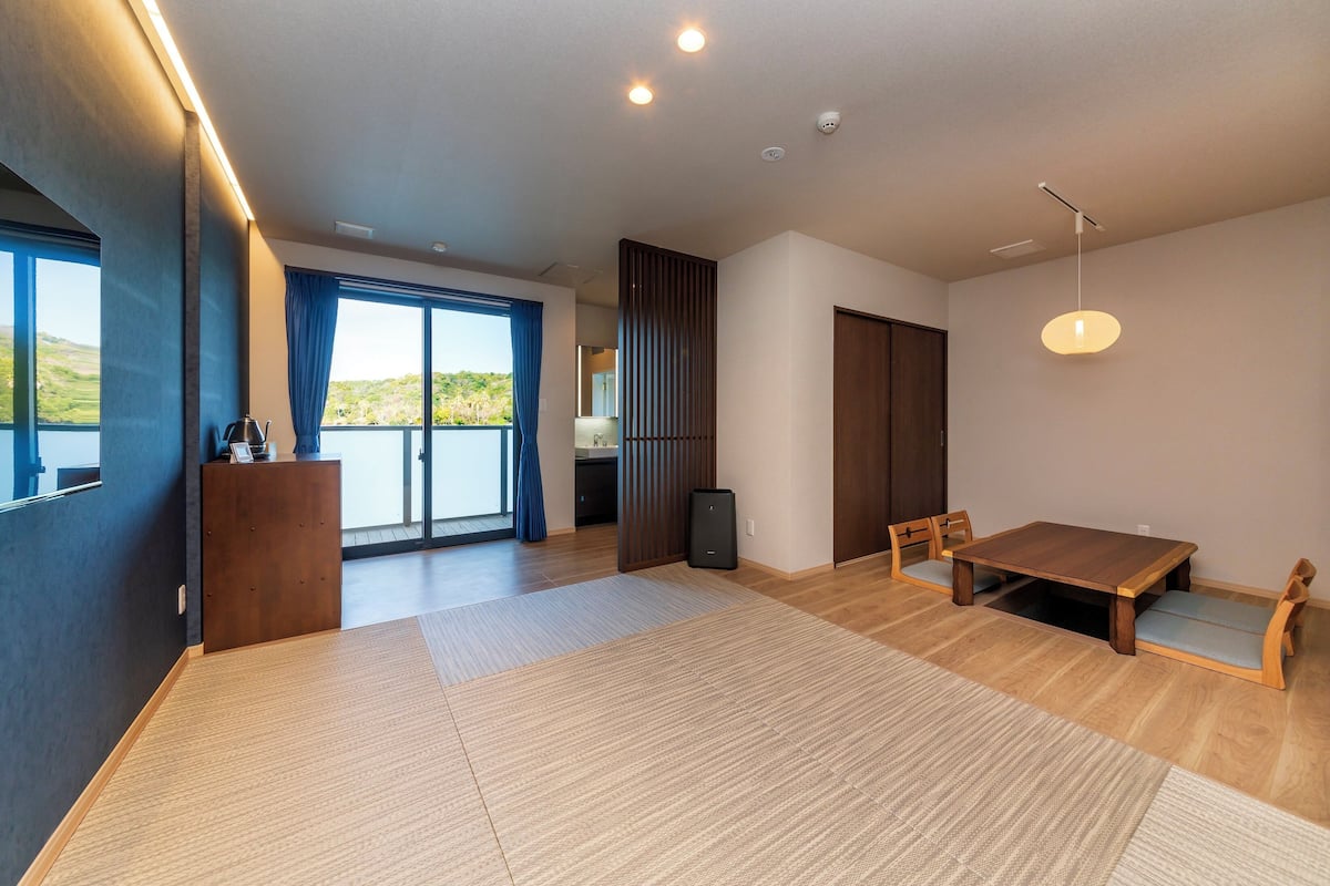 Ein modernes Zimmer mit Holzboden, einem großen Tisch und Blick durch eine Schiebetür.