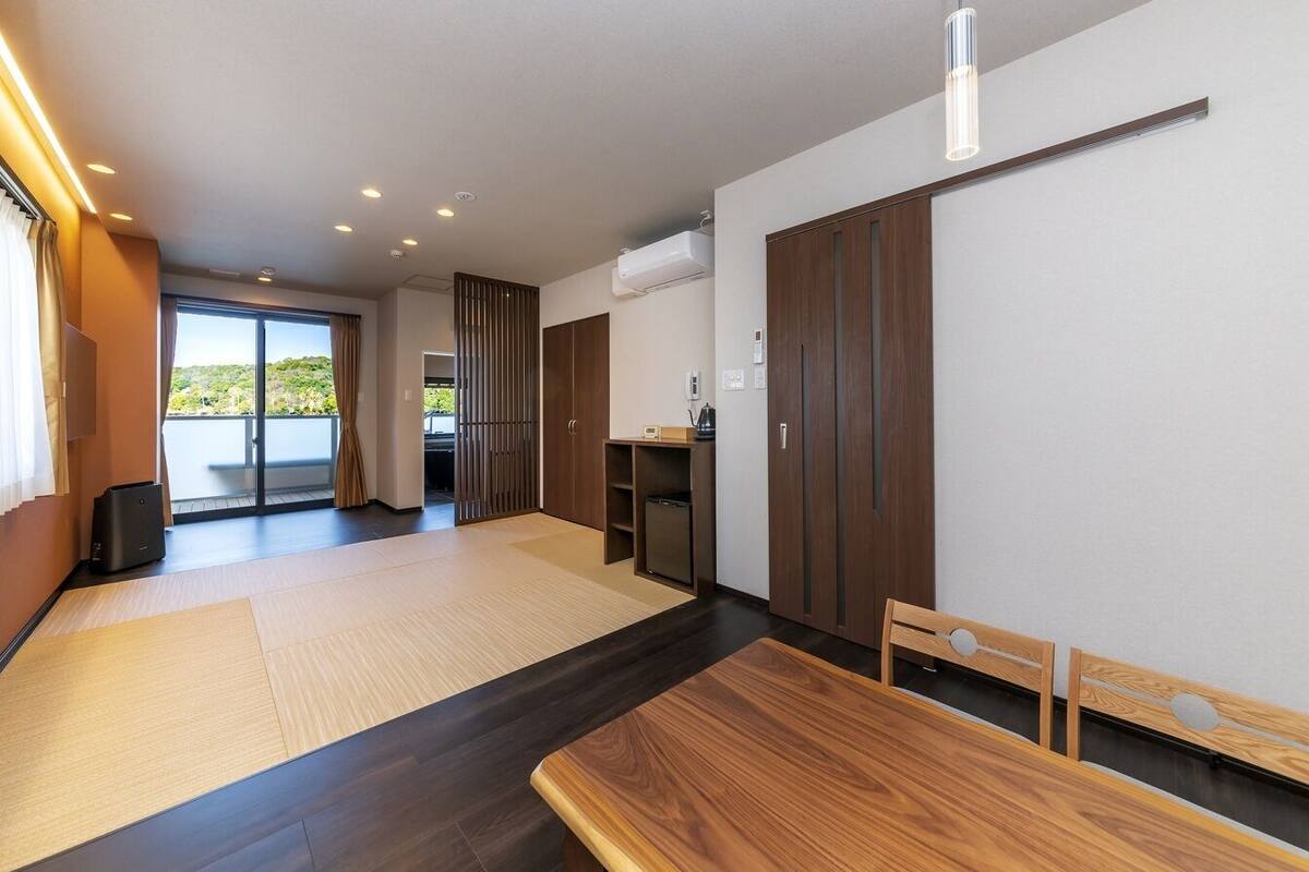 Ein modernes Hotelzimmer mit einer großen Schiebeglasdoor zu einem Balkon, einem Holztisch und einer eingebauten Klimaanlage.