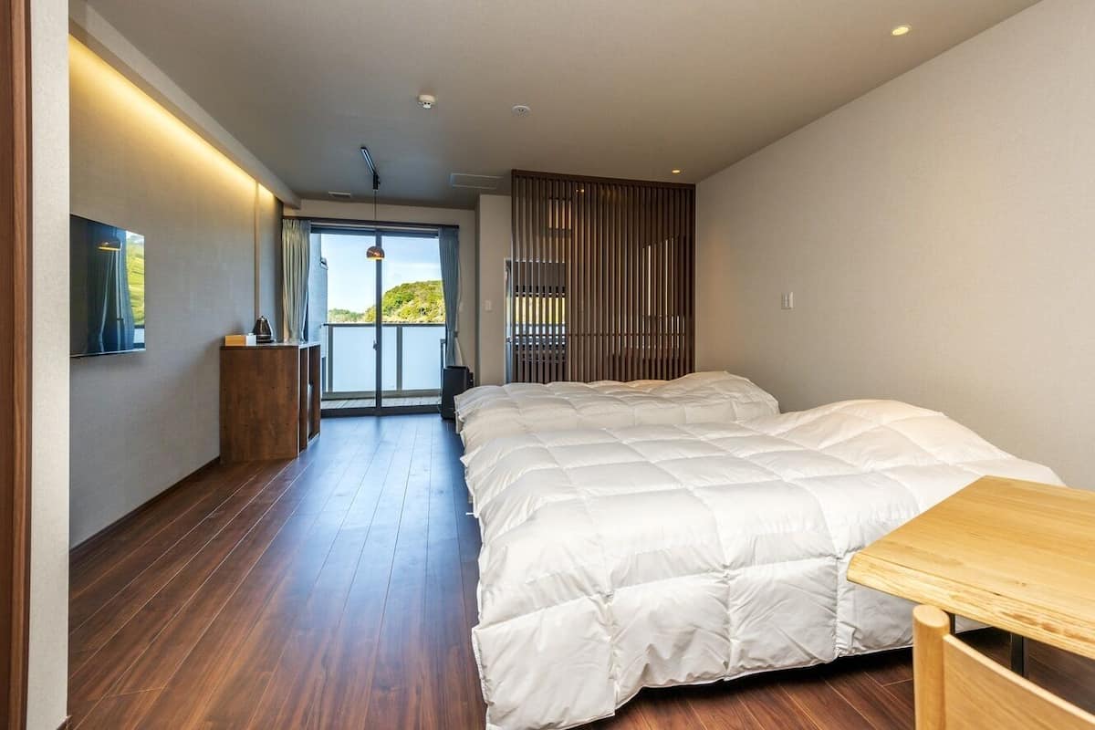 Ein Schlafzimmer mit einem großen Bett, Holzboden, einem kleinen Tisch und Blick ins Freie.