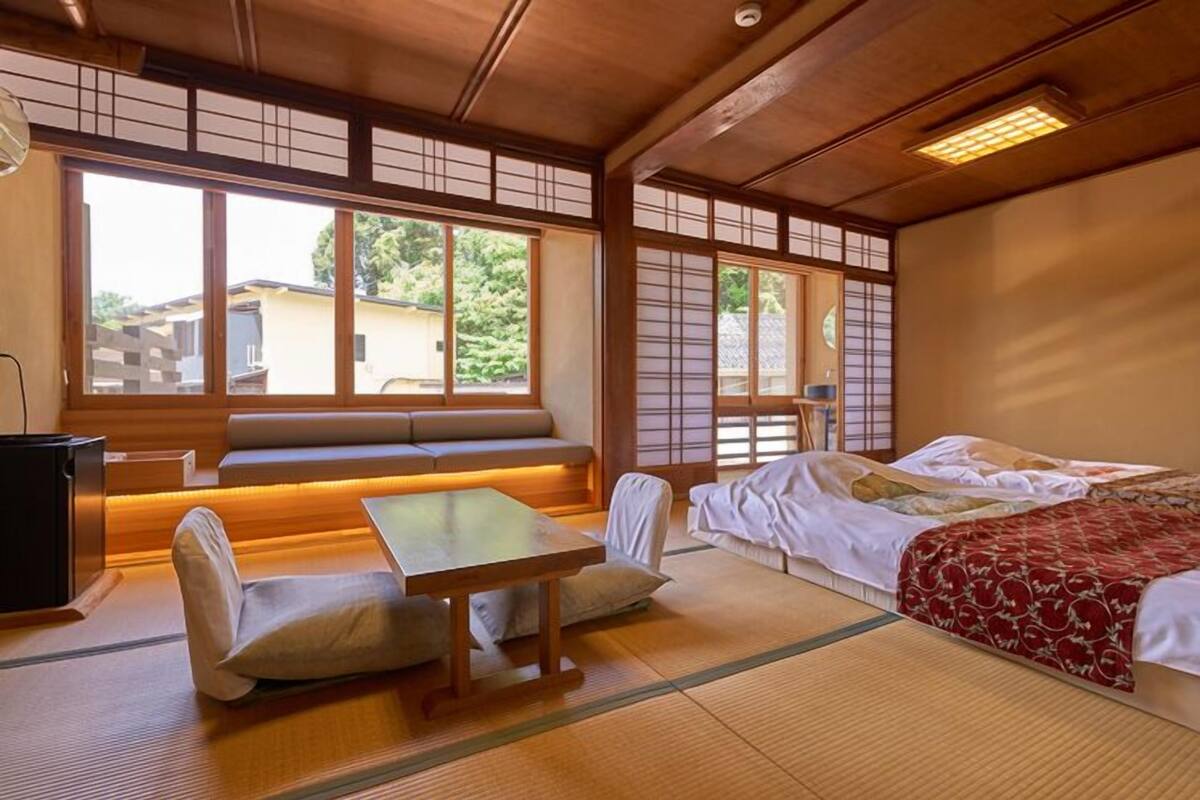 Ett traditionellt japanskt rum med tatamimattor på golvet, ett lågt bord, en soffa och en säng med ett rött, mönstrat överkast.