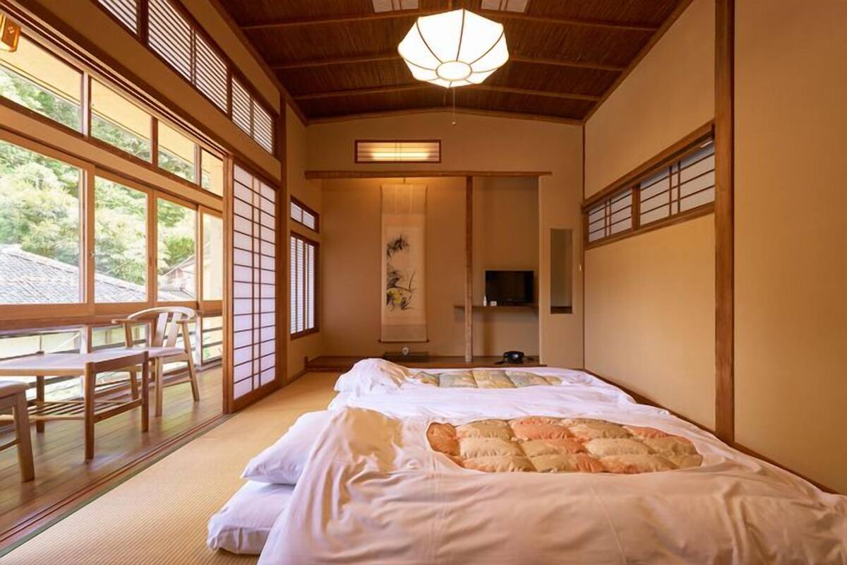 Ett traditionellt japanskt rum med tatamimattor på golvet, en stor säng med ett täcke, ett skrivbord i trä och en tv.