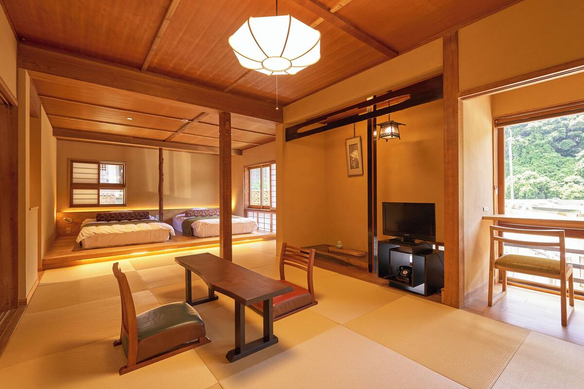 Ett traditionellt japanskt rum med tatamimattor på golvet, en låg säng av trä, en tv och en skjutdörr som leder ut till en balkong.