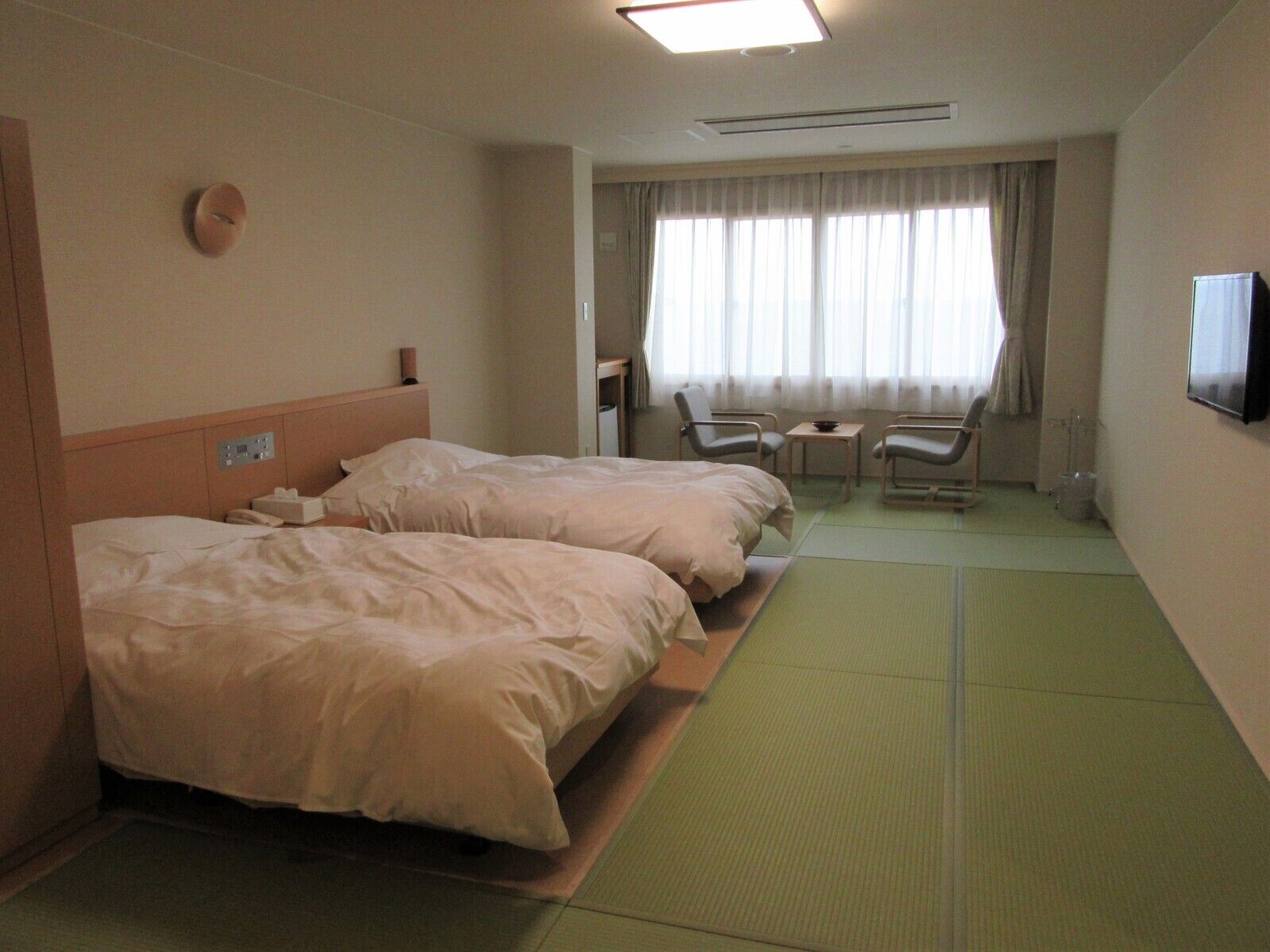 Ein Hotelzimmer mit zwei Betten, einem Fernseher, einem kleinen Tisch und einem Stuhl.