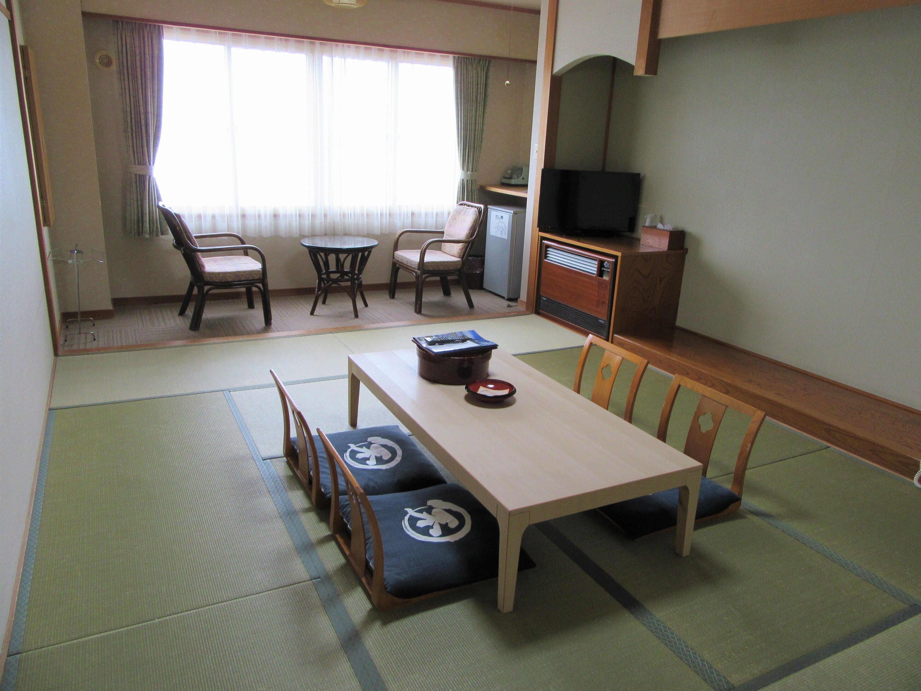 A traditional Japanese-style room with tatami flooring, a low table with cushions, and a television on a wooden cabinet.
