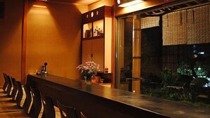 A long bar with chairs, a vase with flowers, and a view of a garden. - Shinkanou Gourmet Ryokan (Izunokuni)