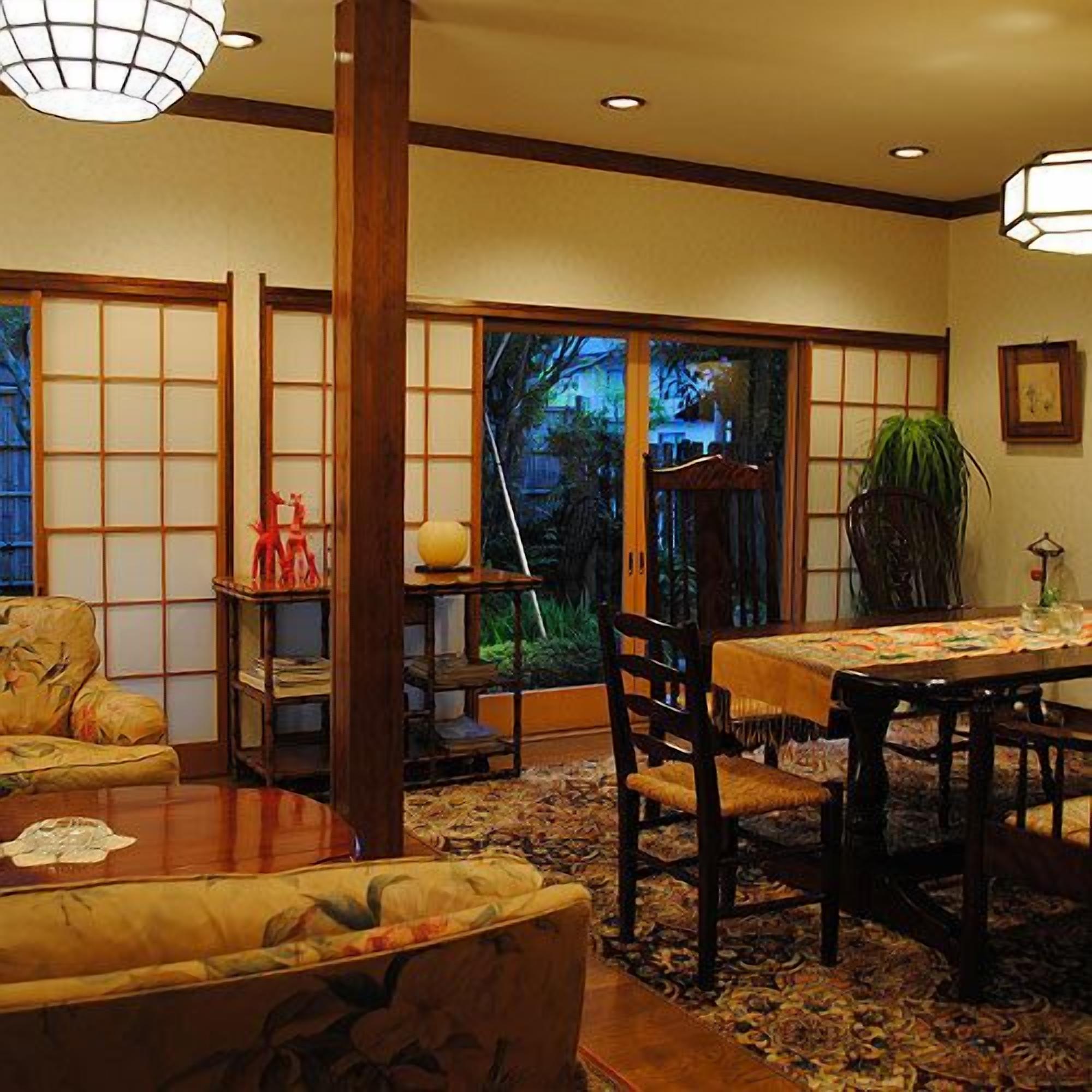 Ein traditioneller japanischer Raum mit Tatami-Boden, einem niedrigen Tisch mit Stühlen und Schiebetüren, die zu einem Garten führen.