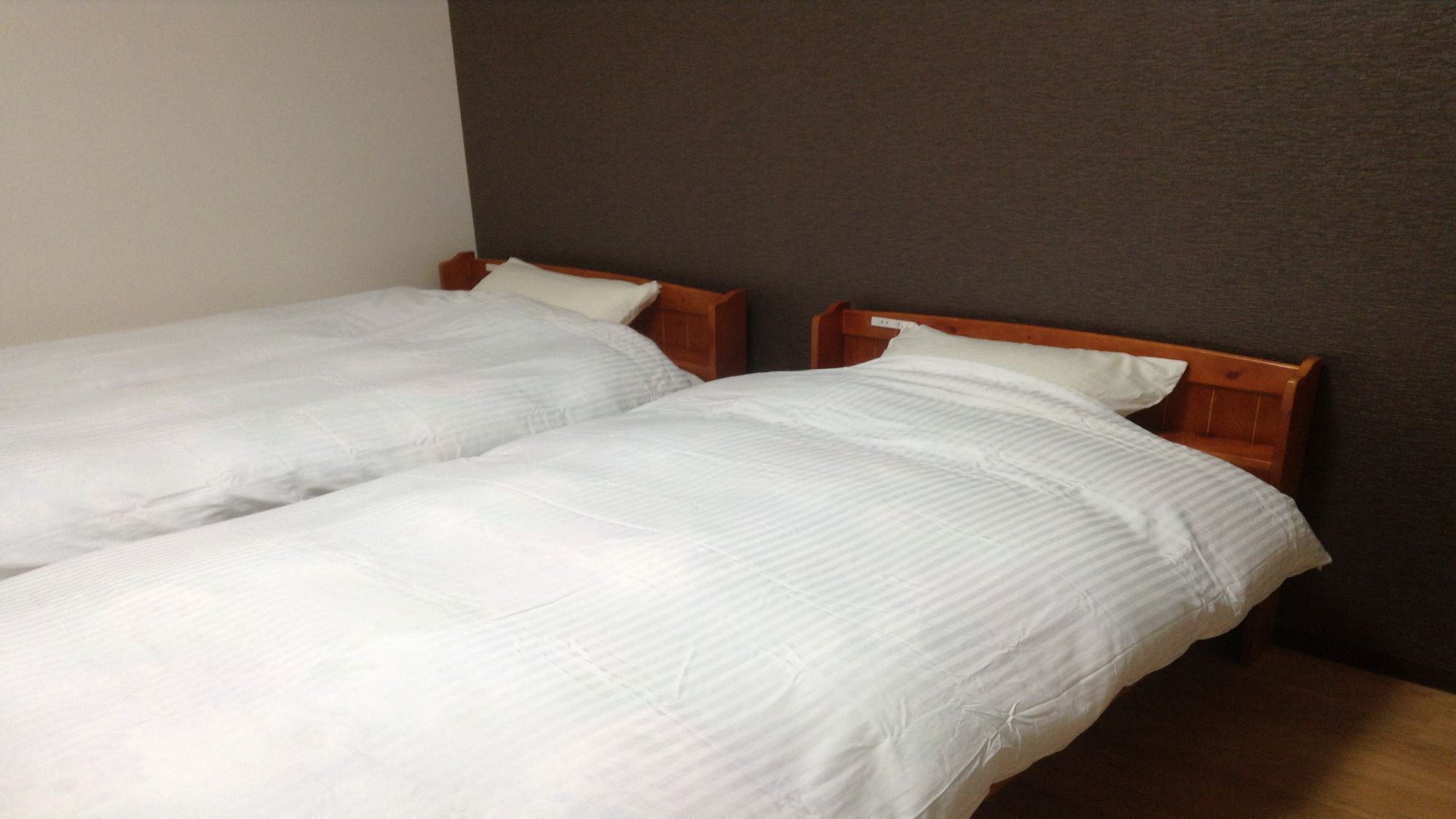 Two single beds with wooden headboards in a room with a plain wall and wooden flooring.