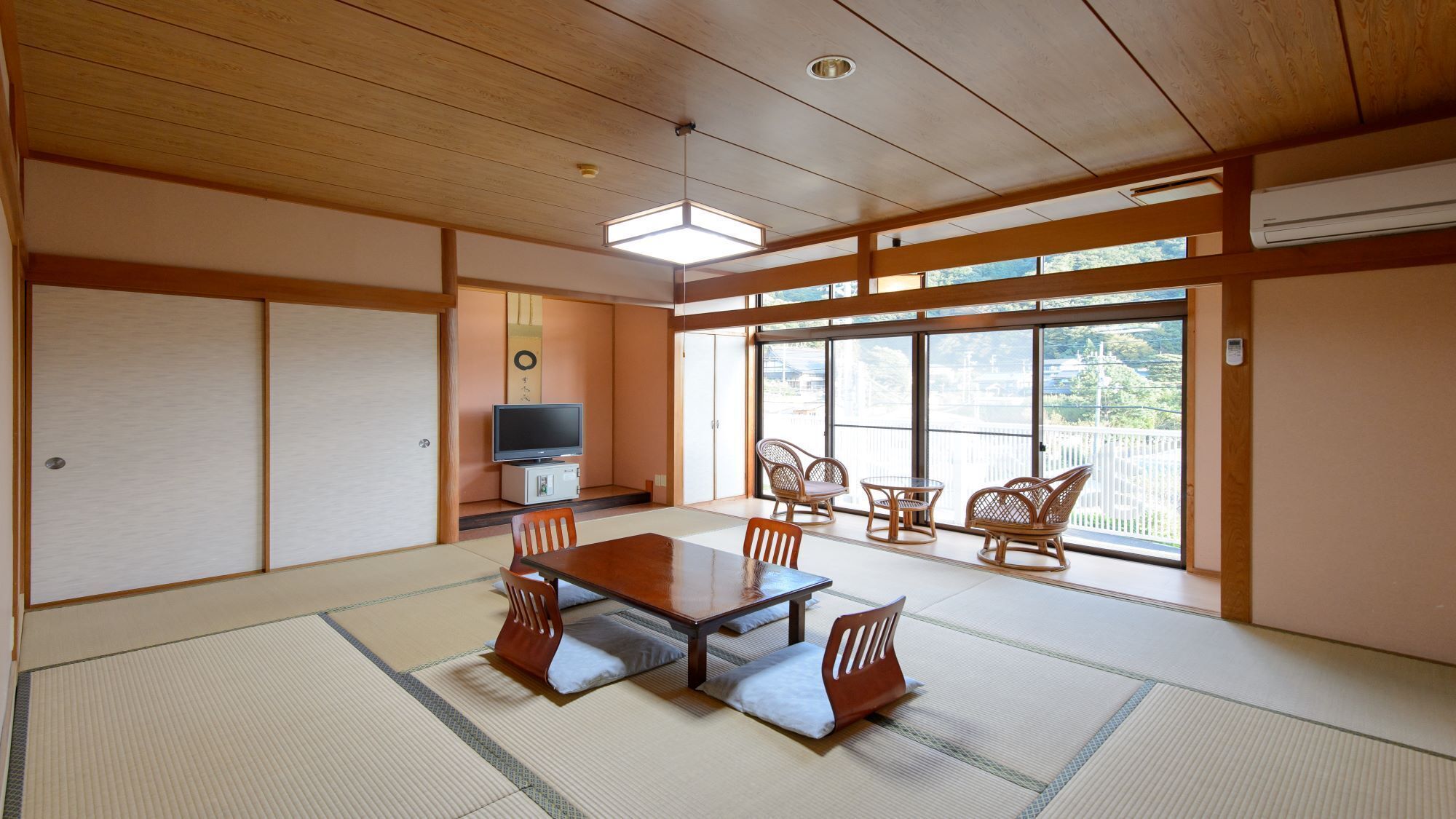 A traditional Japanese room with tatami flooring, a low table with cushions, a television, and a balcony with views.