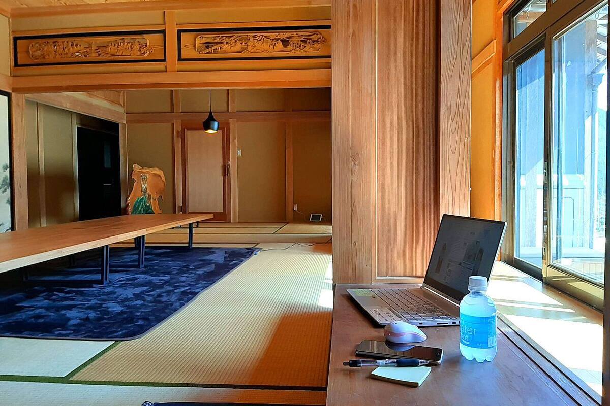 A traditional Japanese room with tatami flooring, a wooden desk with a laptop, a water bottle, and a smartphone.