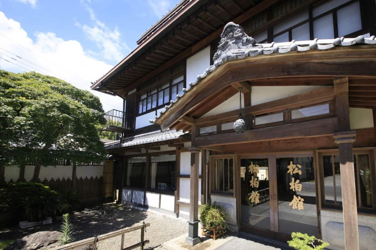 A traditional Japanese building with a wooden structure, a tiled roof, and a small garden area with rocks and plants.
