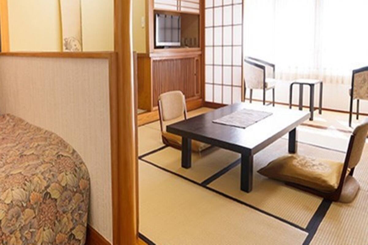 A hotel room with a bed, a dining table, chairs, a TV, and a view of the outside.
