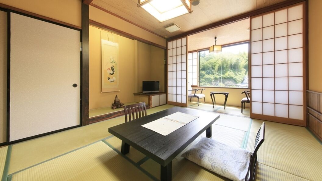 Perinteinen japanilainen huone, jossa on tatamimatto, matala pöytä ja pehmuste, liukuvat ovet ja näkymä vehreään maisemaan.