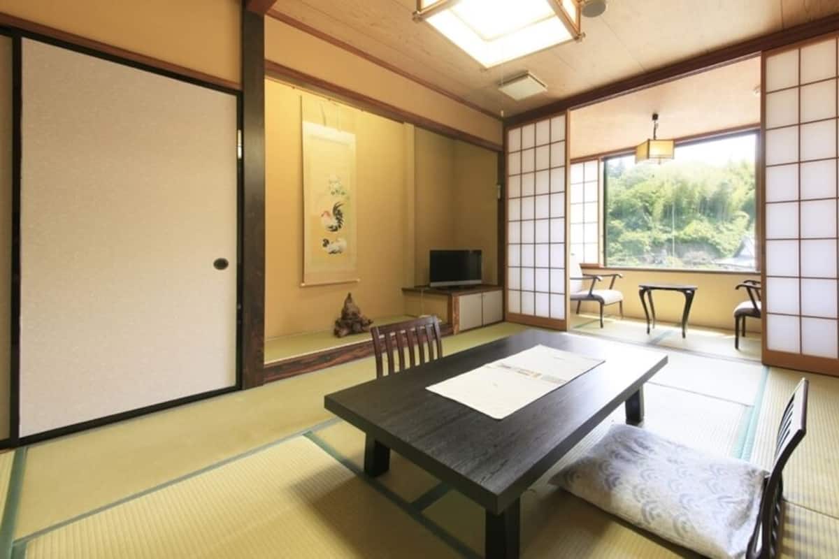 A traditional Japanese room with tatami flooring, a low table with a cushion, sliding doors, and a view of greenery outside.