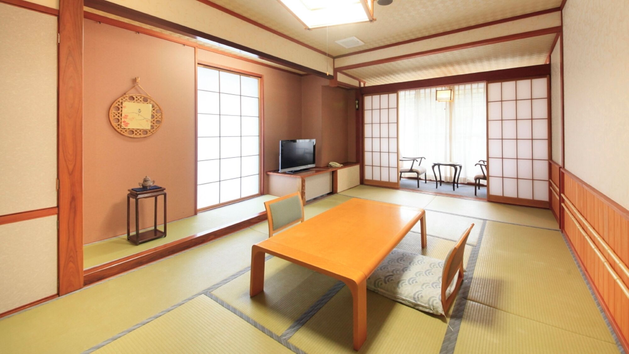 Perinteinen japanilaistyylinen huone, jossa on tatamimatto, matala pöytä, tuoleja, televisio ja liukuvat ovet.