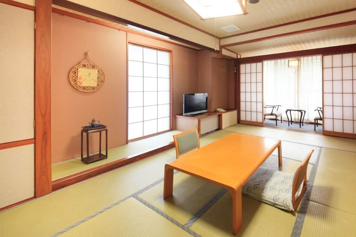 A traditional Japanese-style room with tatami flooring, a low table, chairs, a television, and sliding doors.