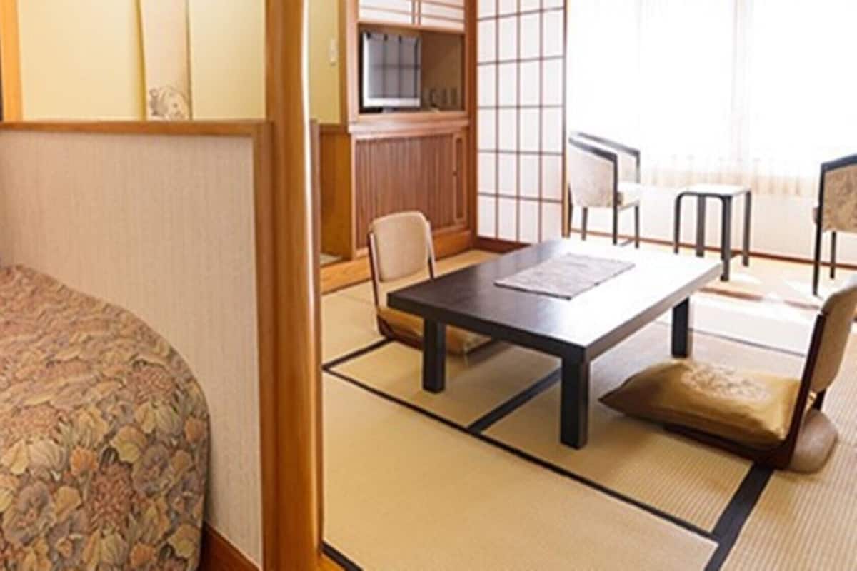 A hotel room with a bed, a dining table, chairs, a TV, and a view of the outside.