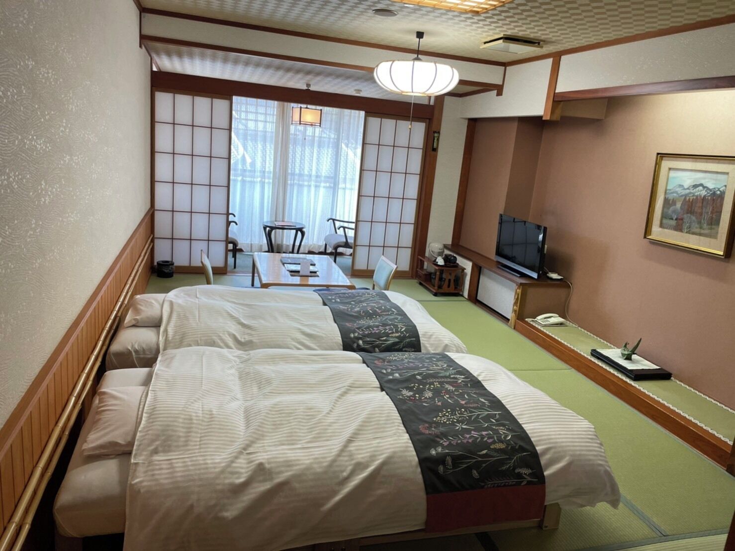 Hotellihuone, jossa on kaksi sänkyä, televisio, työpöytä ja perinteinen japanilainen liukuovi.