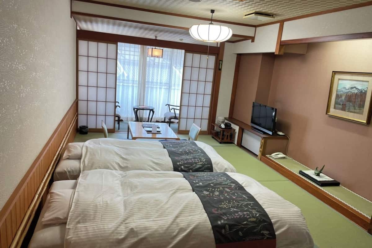 A hotel room with two beds, a television, a desk, and a traditional Japanese sliding door.