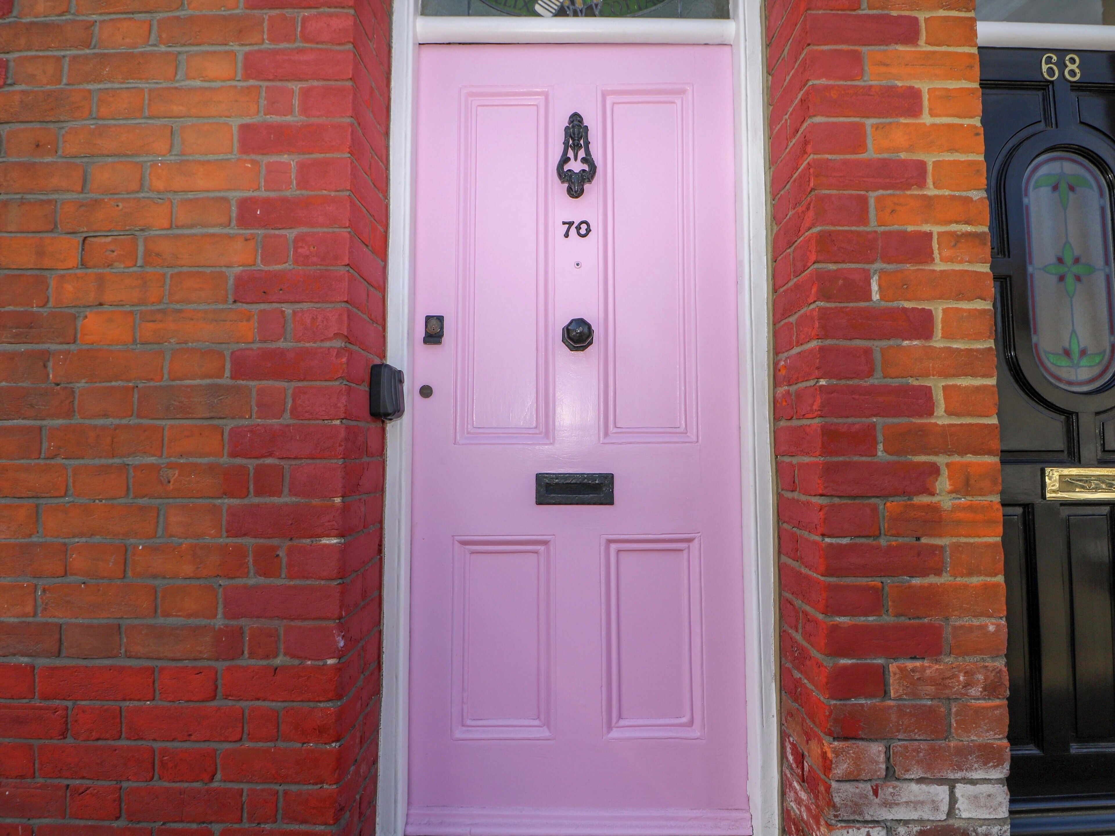 A pink door with the number 70, a black doorbell, and a black door with the number 68.