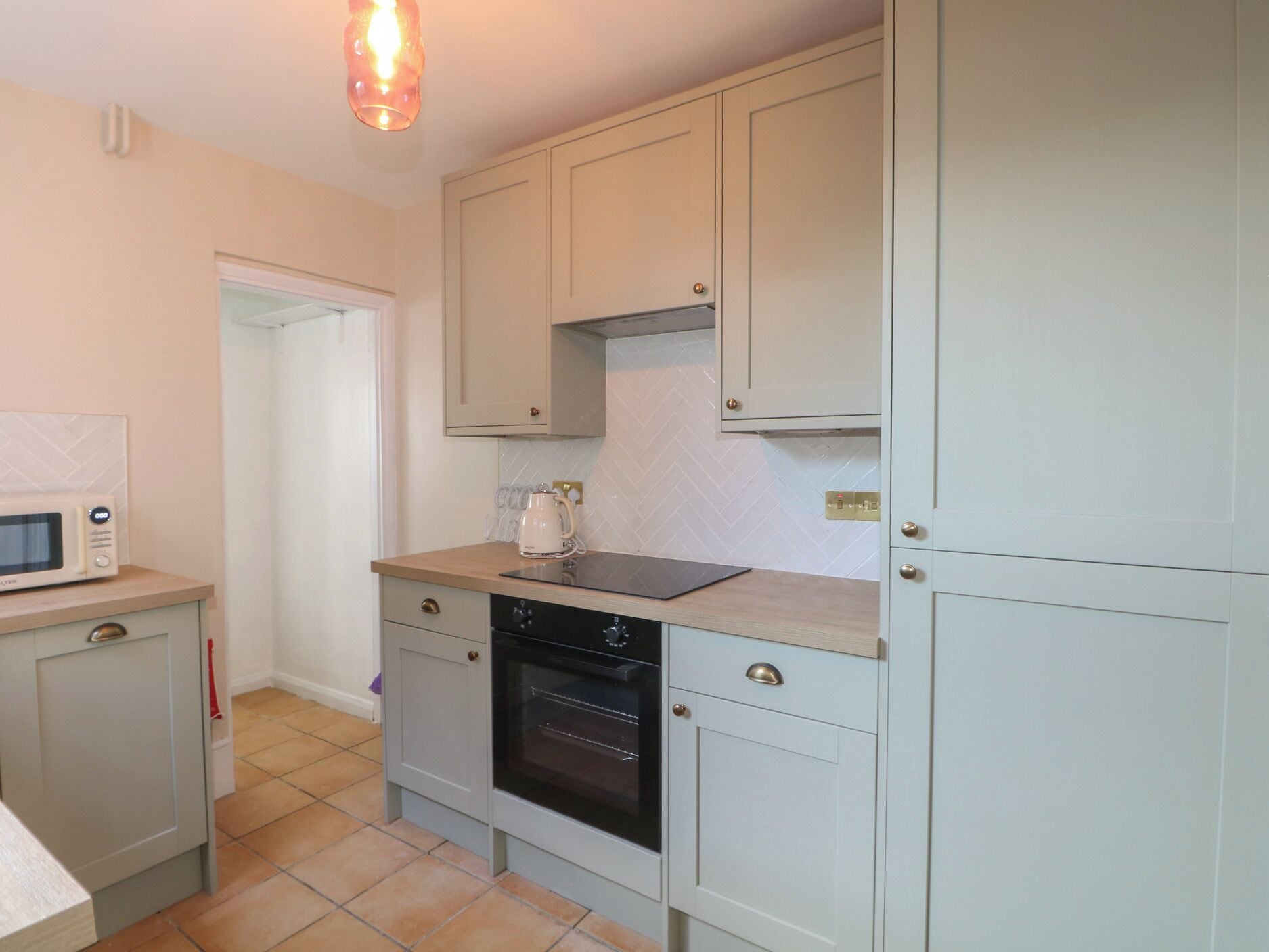 A compact kitchen with a microwave, oven, and a kettle on the countertop.