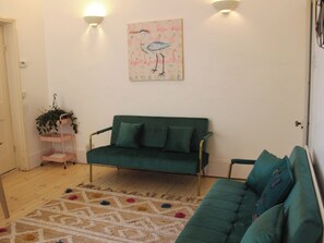 Un salon avec un canapé vert, un tapis à motifs et une œuvre d’art représentant un oiseau, accrochée au mur.