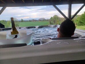 Un jacuzzi con una botella de champán, rodeado por una estructura de madera y vistas a un paisaje verde.