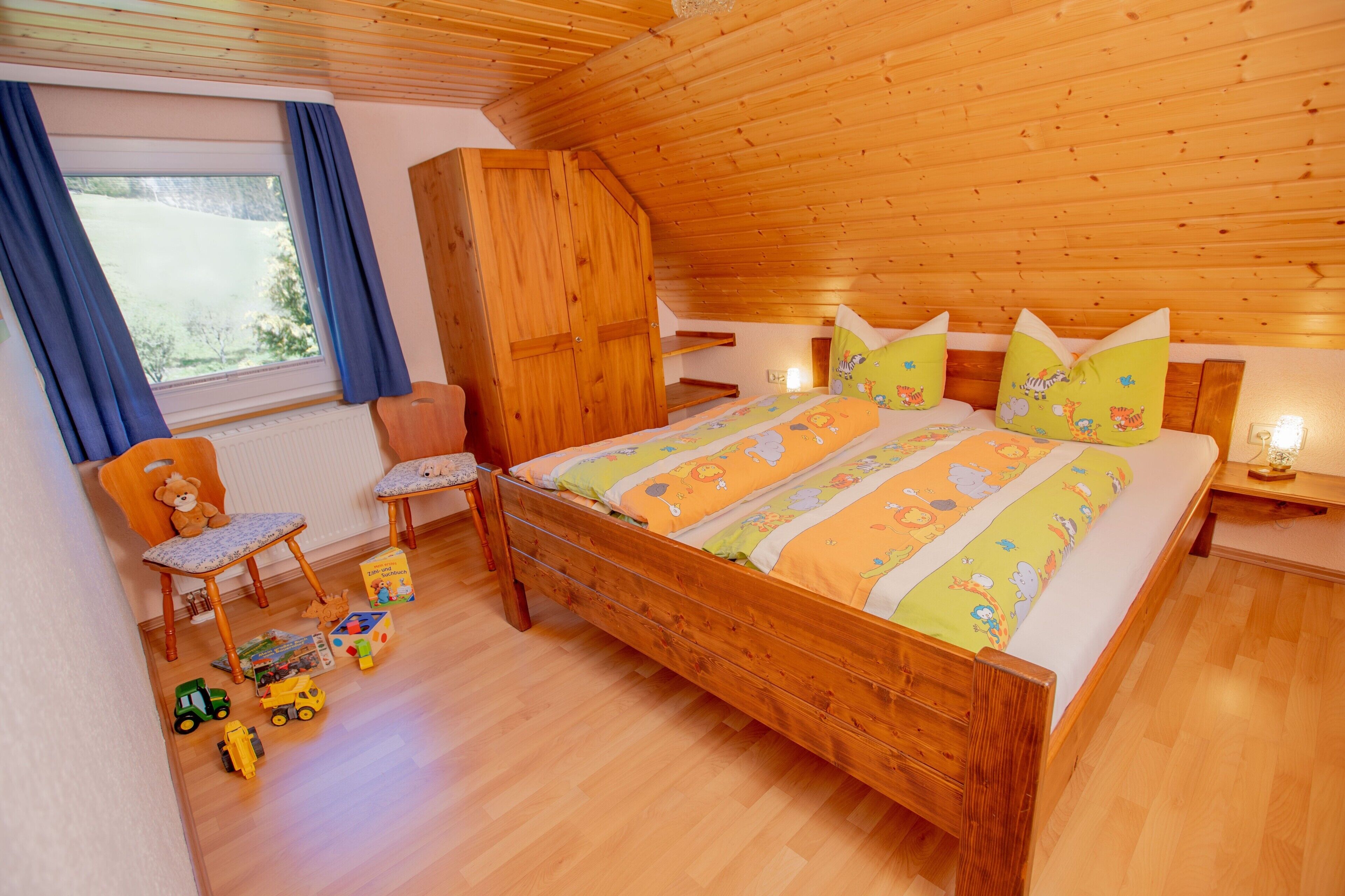 Un dormitorio de madera con una cama, una silla y juguetes en el suelo.