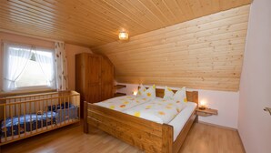 Un dormitorio con una cama litera de madera, una cama individual con ropa de cama floral, un armario de madera y una ventana con cortinas.