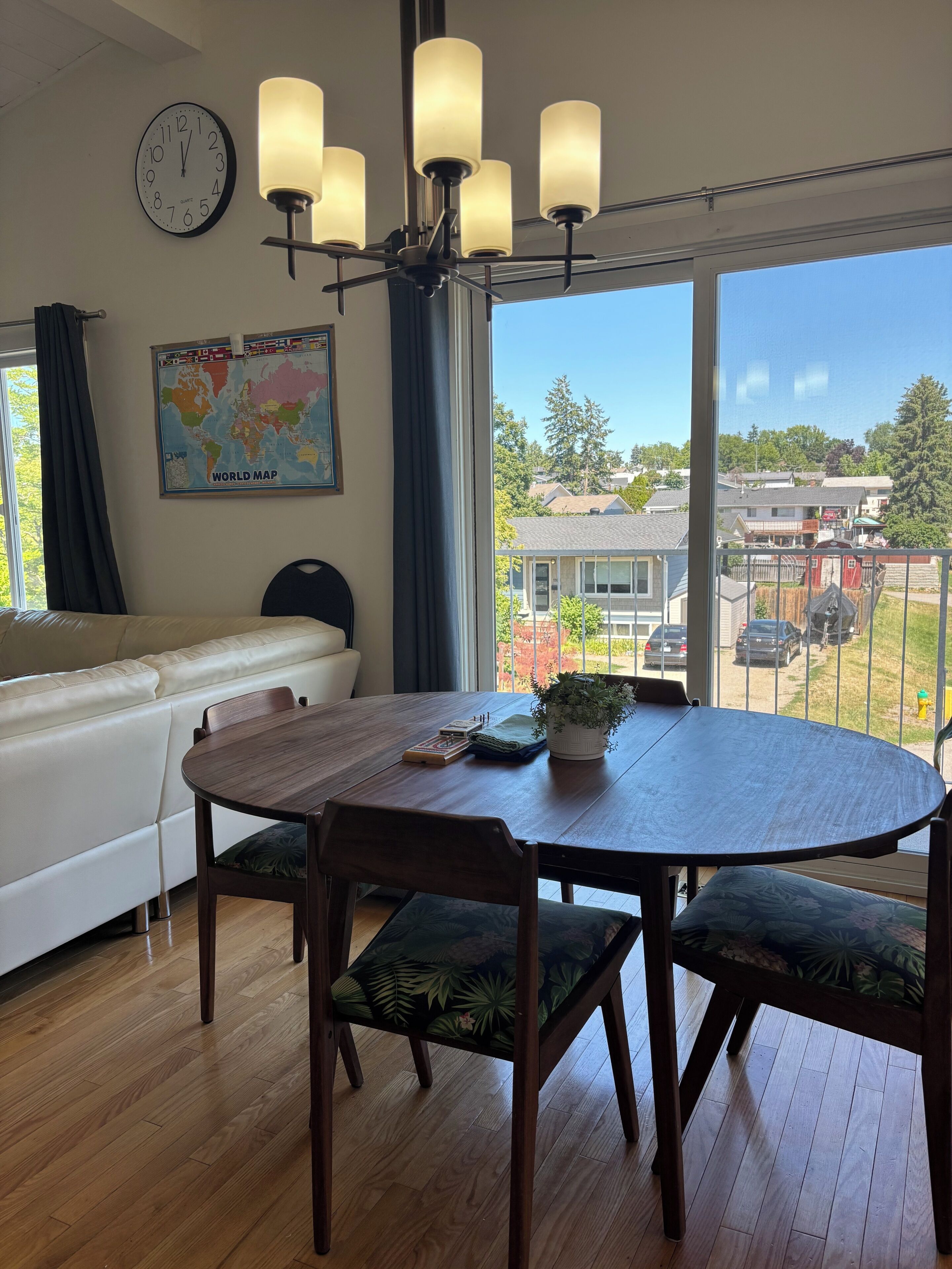 Une pièce comprenant une table à manger en bois, des chaises, une carte du monde, une horloge et une vue sur l’extérieur.
