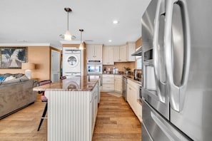 A modern kitchen with a central island, stainless steel appliances, and a dining area with a sofa. - Coconut Breeze (Panama City Beach)