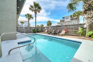 A swimming pool with a wooden fence, lounge chairs, and palm trees. - Coconut Breeze (Panama City Beach)