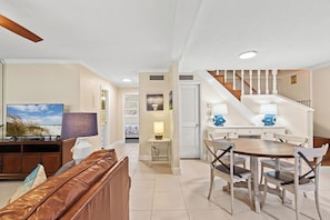 A living room with a TV, sofa, and dining area with chairs and a table. - Coconut Breeze (Panama City Beach)
