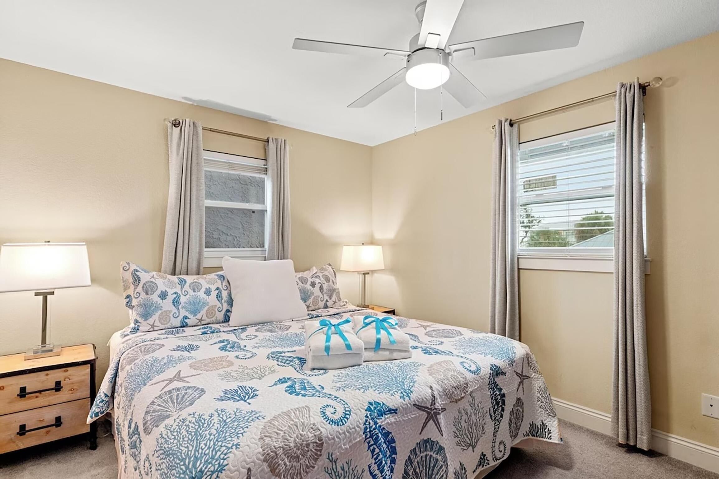 A bedroom with a bed, two bedside lamps, a ceiling fan, and a window with curtains.
