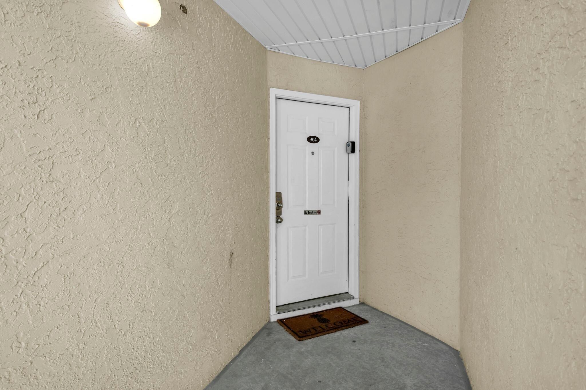 A white door with a number plate, a doormat, and a light fixture above.