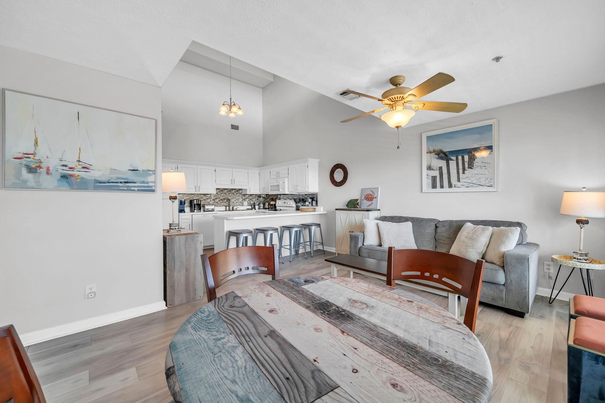A modern kitchen with white cabinets, a dining area with a wooden table, and a gray sofa.
