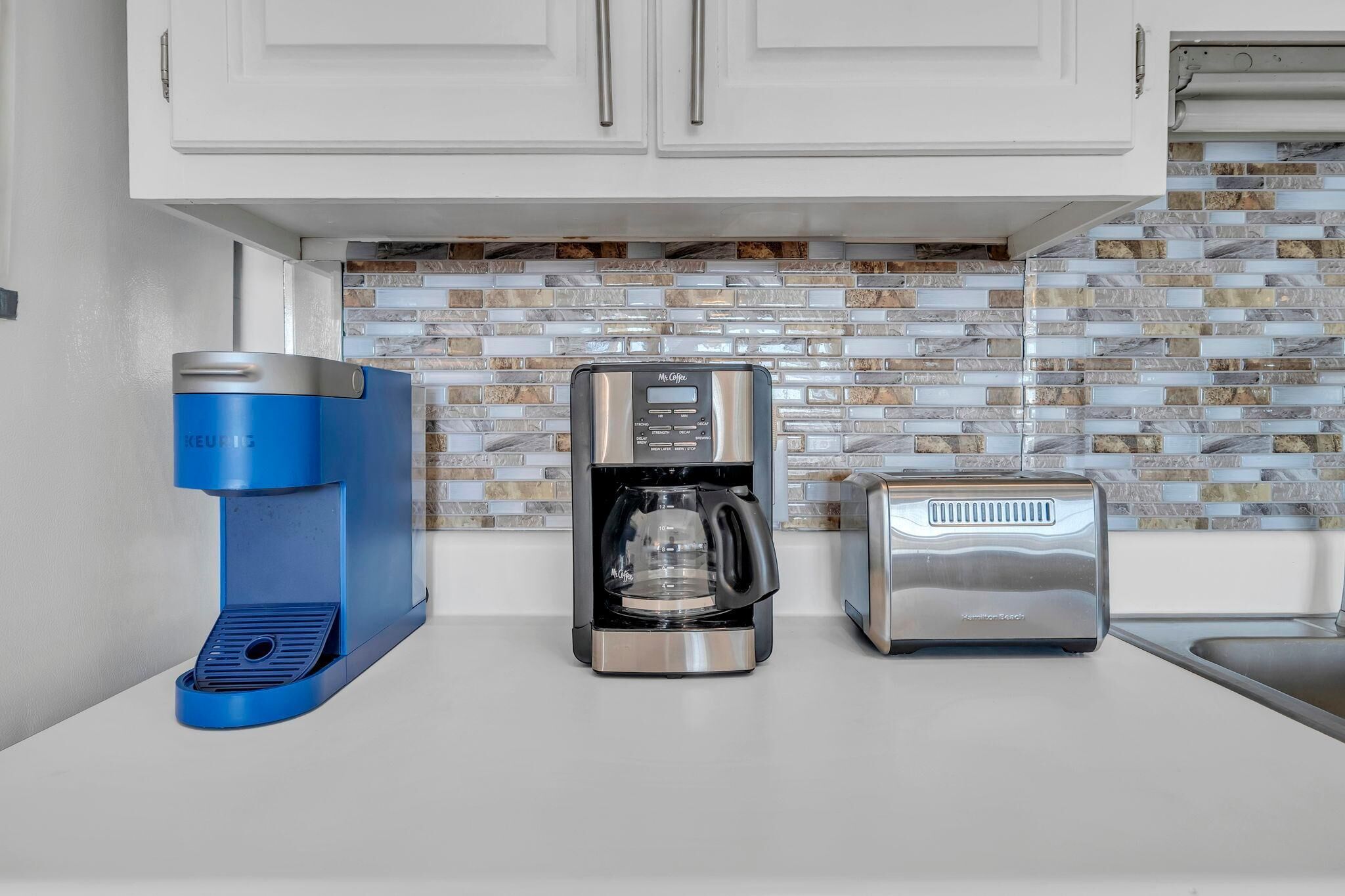A kitchen with a coffee maker, a coffee pot, and a toaster.